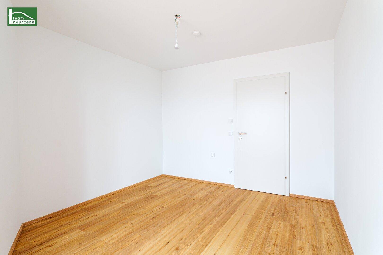 Leerer Raum mit weißer Tür und hellem Laminatboden, ideal für Schlafzimmer oder Büro.