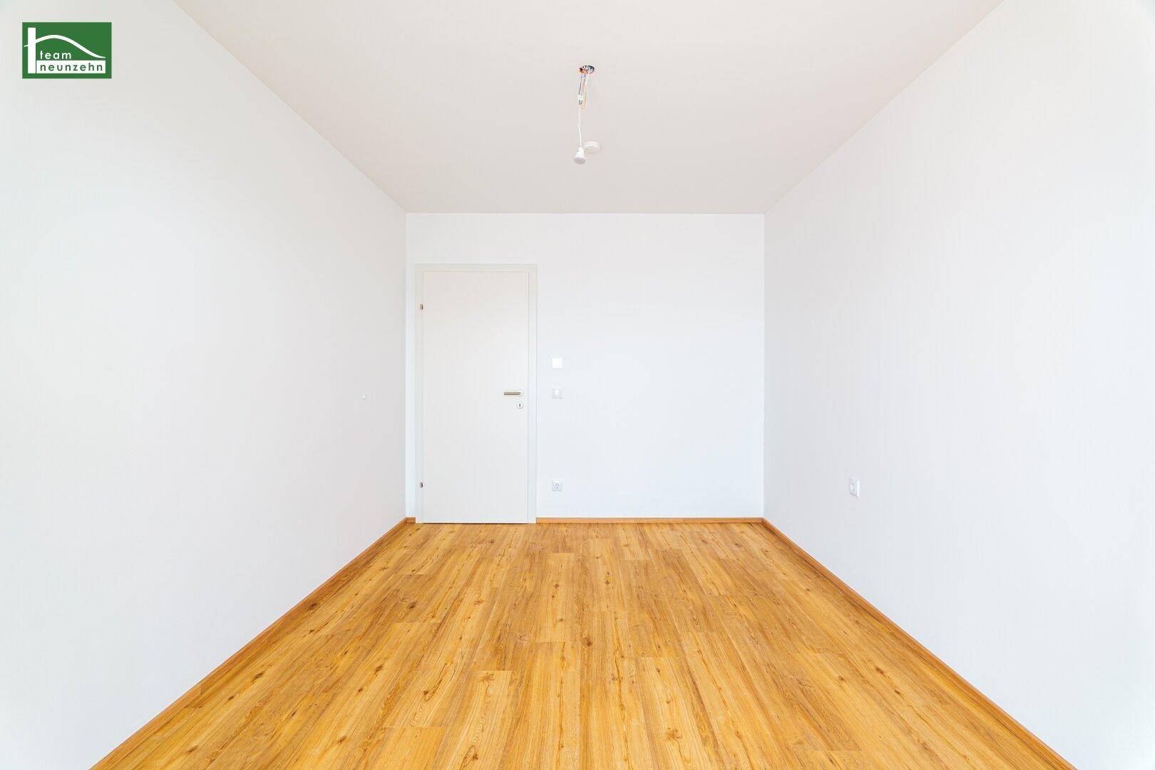 Leerer Raum mit hellem Laminatboden und weißer Tür, bereit zur individuellen Gestaltung.