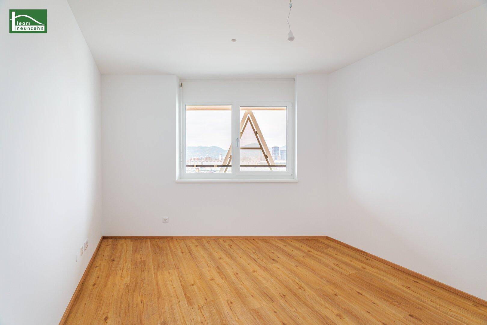 Helles Schlafzimmer mit Parkettboden und weitem Ausblick durch das Fenster.