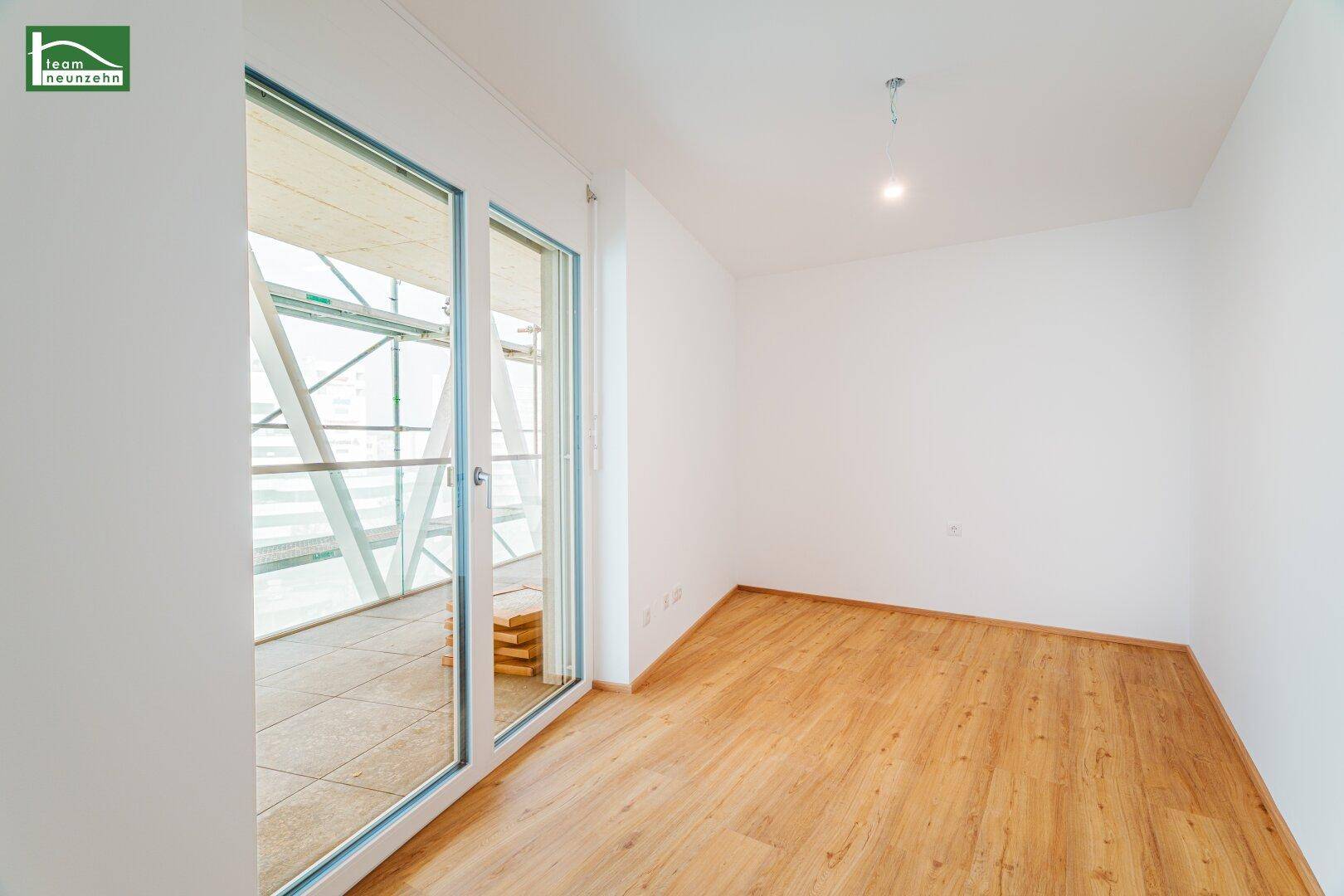Leeres Zimmer mit hellem Parkettboden und großen Fenstern, die viel Licht spenden.