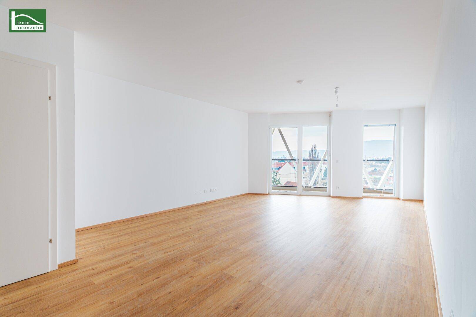 Geräumiger, heller Wohnraum mit großen Fenstern und Zugang zu einem Balkon.