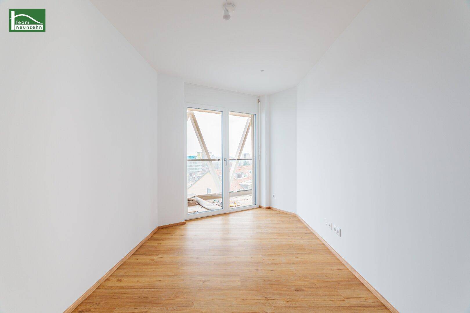 Helles Schlafzimmer mit Balkonzugang und Laminatboden, viel Tageslicht durch große Fenster.