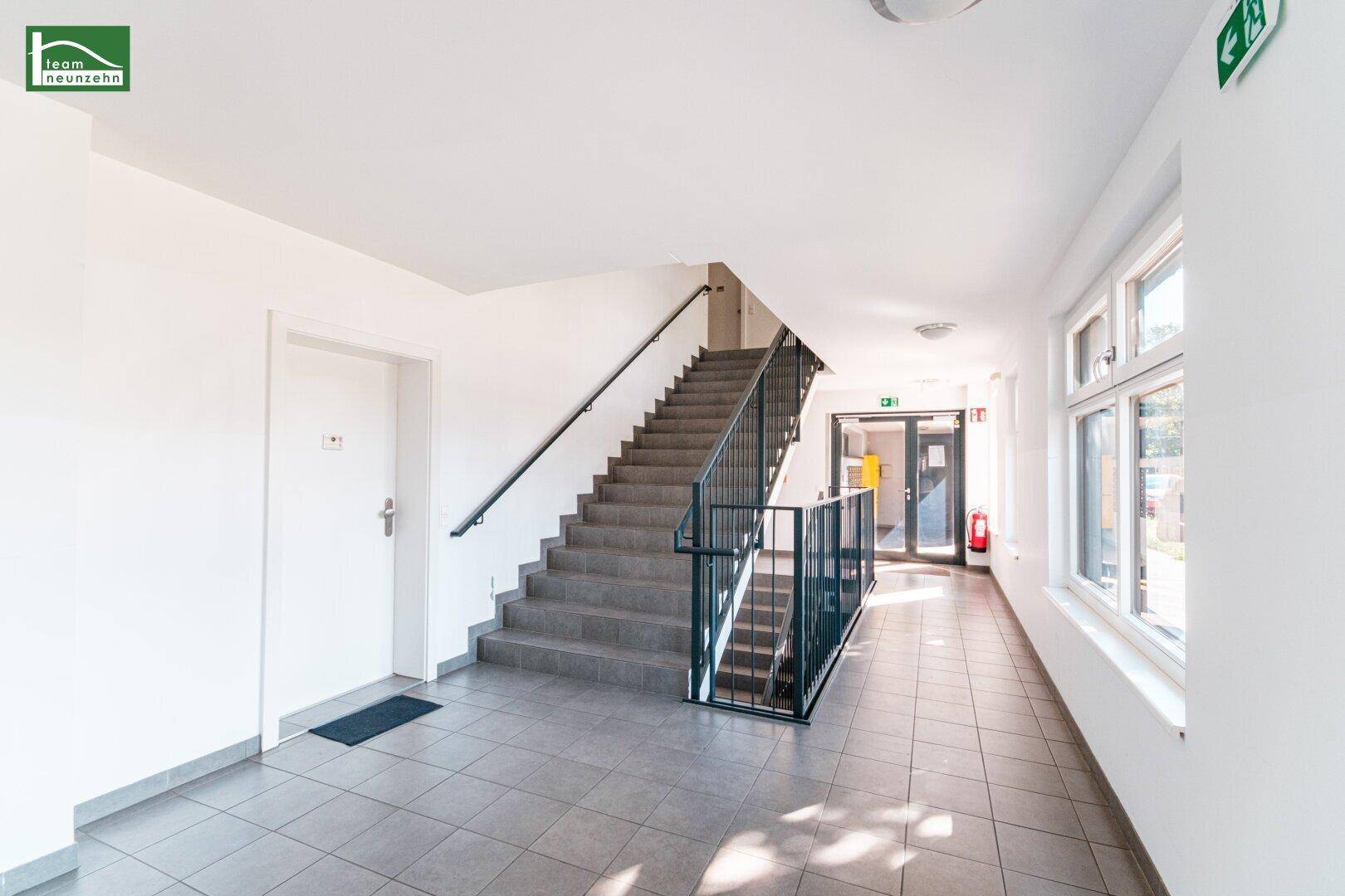 Heller Treppenaufgang mit Fliesenboden und großen Fenstern für natürliches Licht.