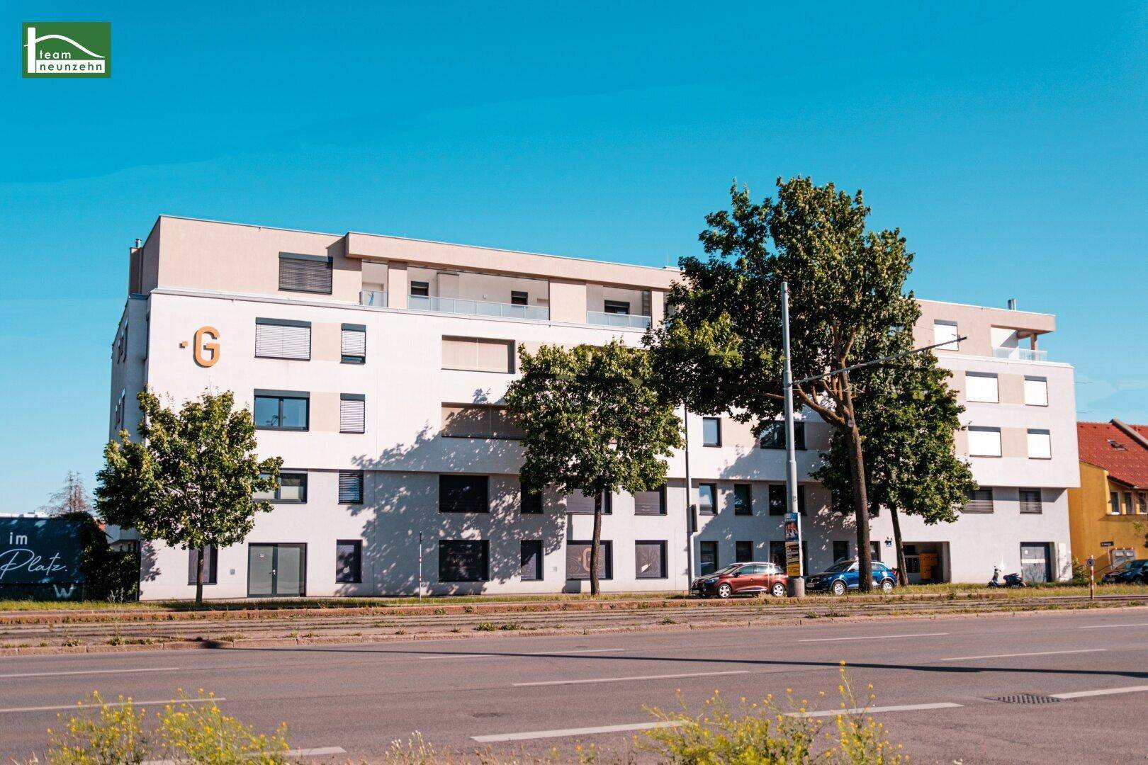Modernes Mehrfamilienhaus mit weißer Fassade und großen Fenstern an einer Straße gelegen.