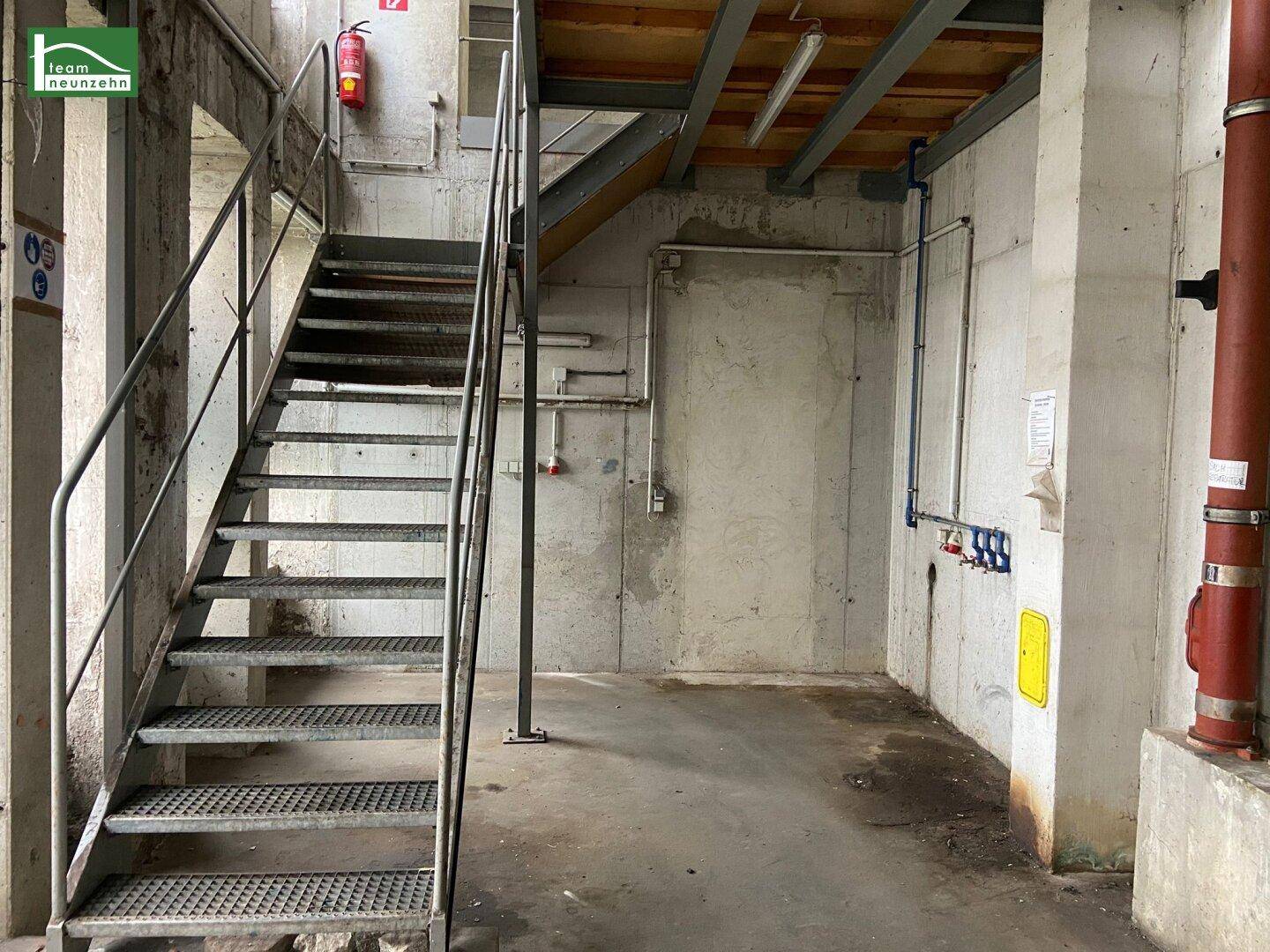 Industrielle Metalltreppe in einem Bereich mit rohen Betonwänden und sichtbaren Leitungen.