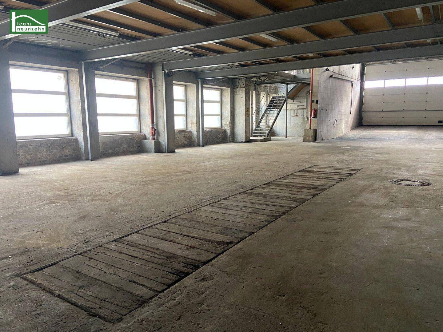 Weitläufiger Industrieraum mit Betonboden, vielen Fenstern und einer langen Grube im Boden.