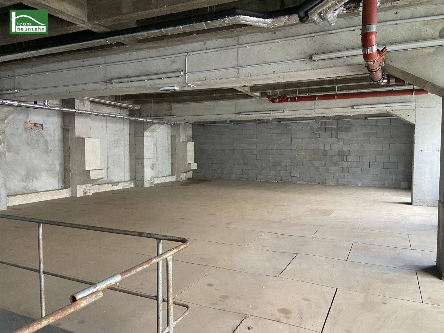 Untergeschoss mit Betonwänden, Holzplattenboden und sichtbaren Rohren an der Decke.