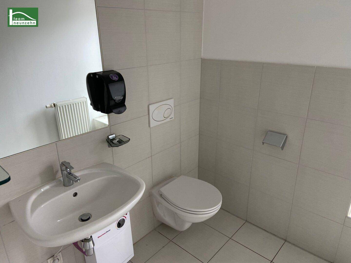 Kleines, gefliestes Gäste-WC mit Waschbecken, Toilette und Spiegel.