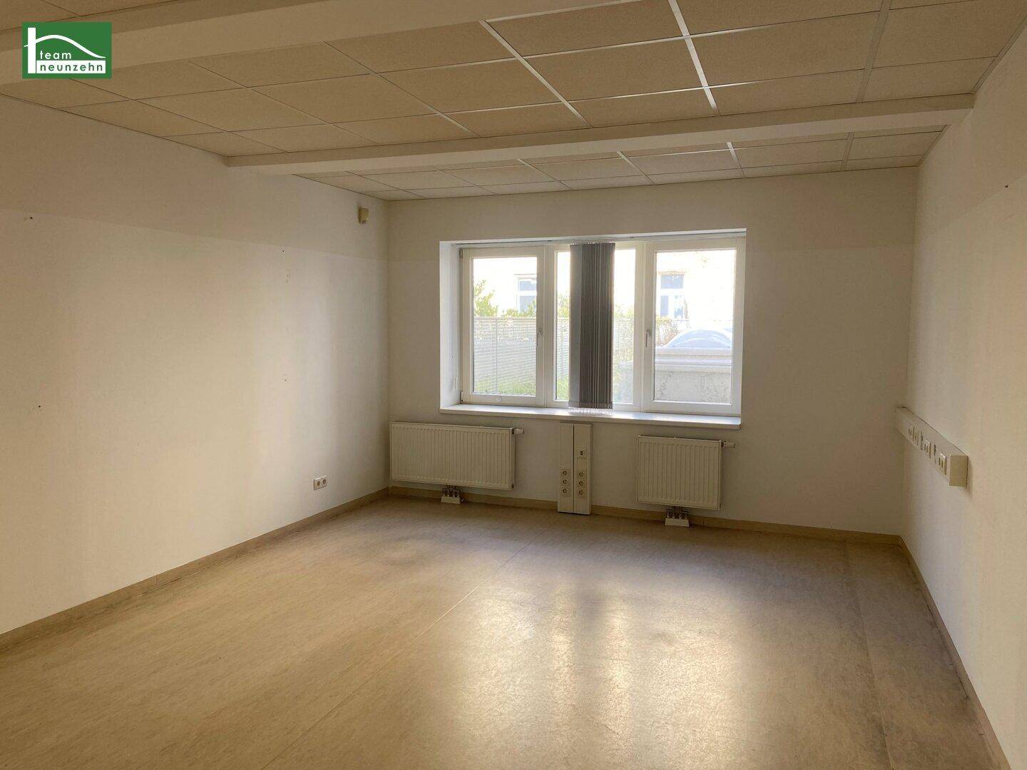 Helles Büro mit Laminatboden, großen Fenstern und Blick ins Grüne.