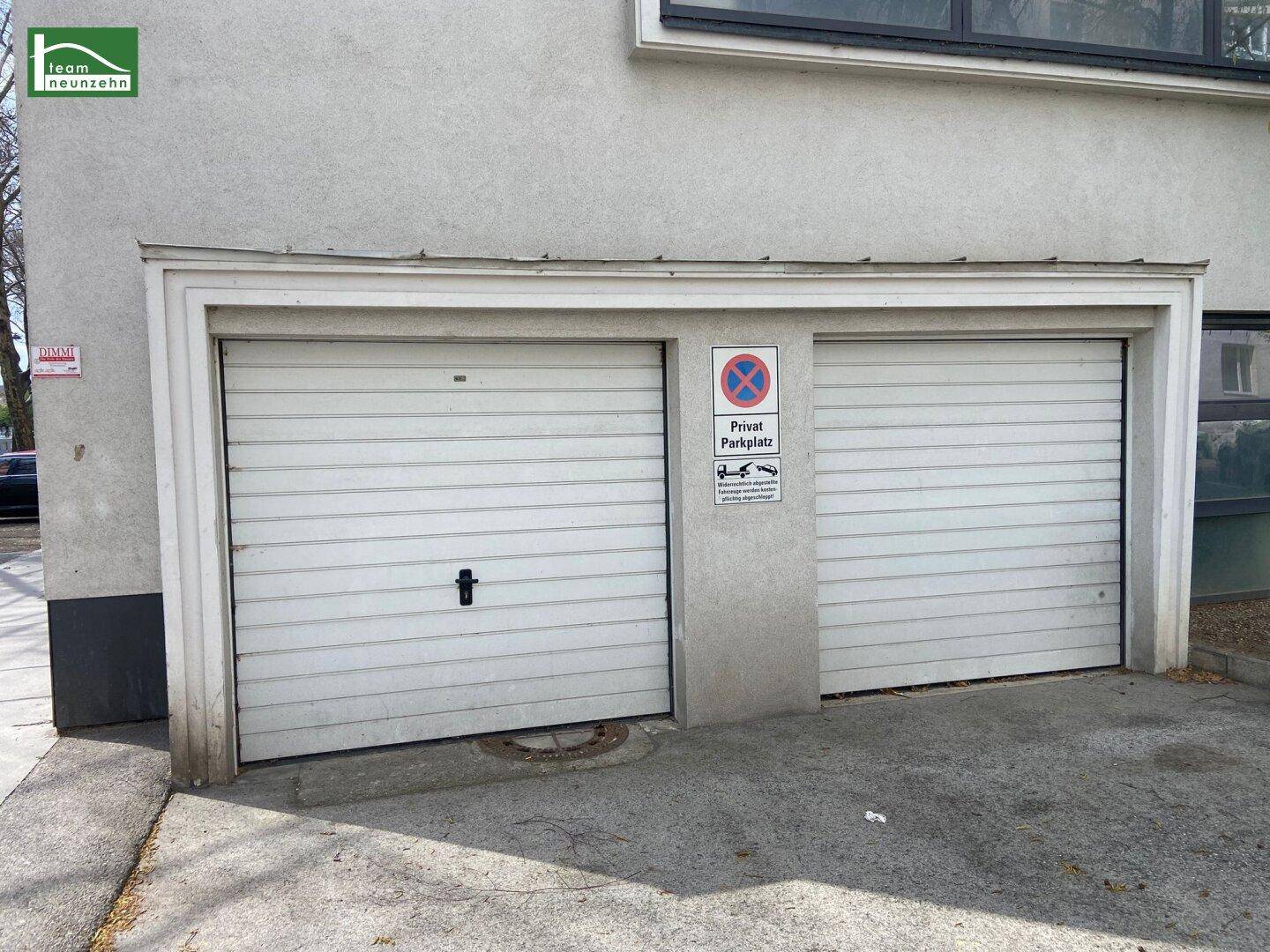 Zwei Garagentore an der Gebäudefassade mit einem privaten Parkplatzschild.