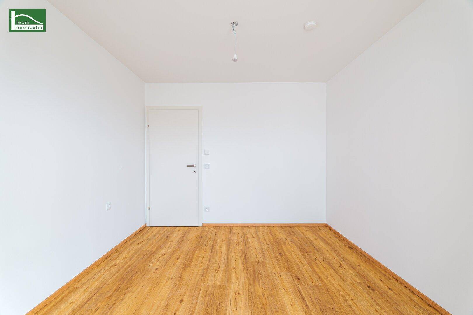 Leerer Raum mit hellem Laminatboden und weißer Tür, bereit zur individuellen Gestaltung.