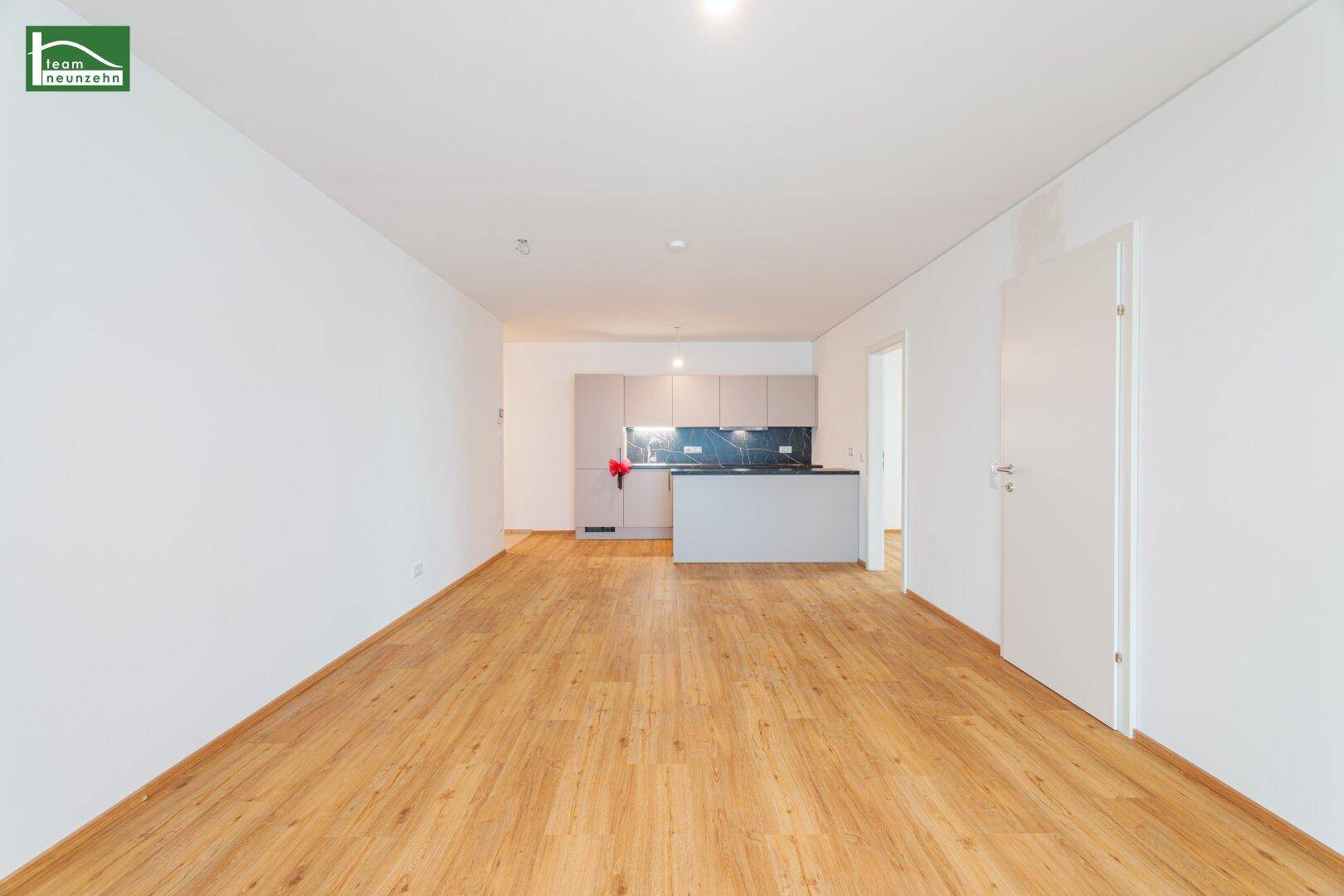 Weitläufige, unmöblierte Wohnküche mit hellem Laminatboden und viel Tageslicht.