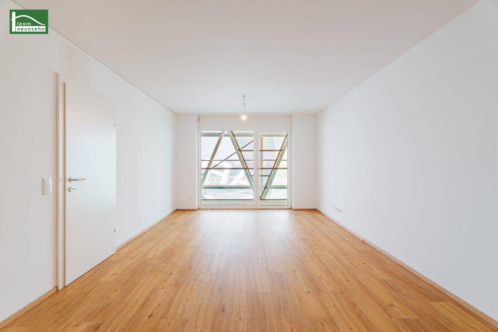 Heller, unmöblierter Raum mit großen Fenstern und durchgehendem Laminatboden.