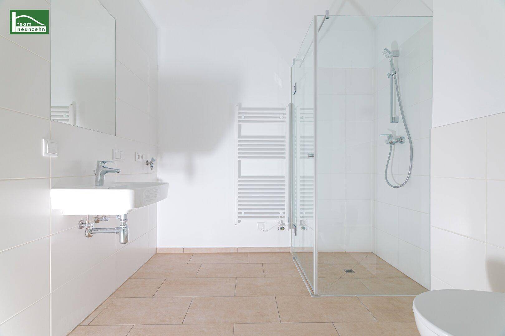 Modernes Badezimmer mit ebenerdiger Dusche, weißem Waschbecken und hellen Fliesen.