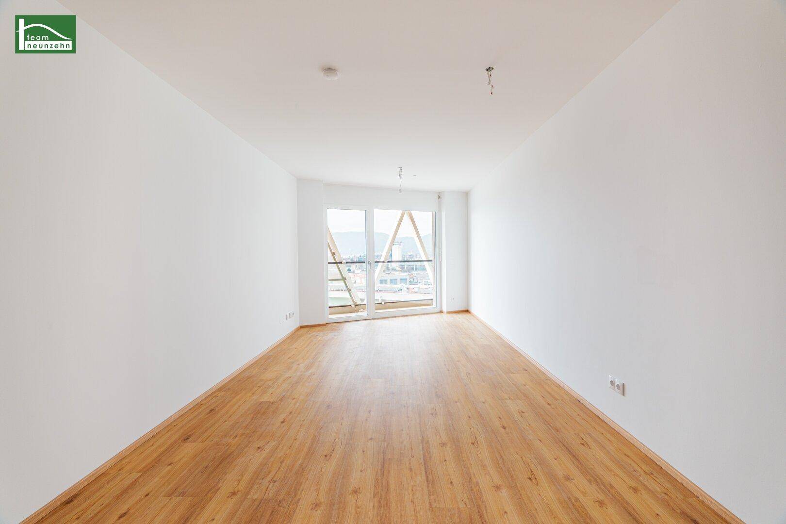 Geräumiger, heller Wohnbereich mit Holzboden und Zugang zu einem Balkon oder einer Terrasse.