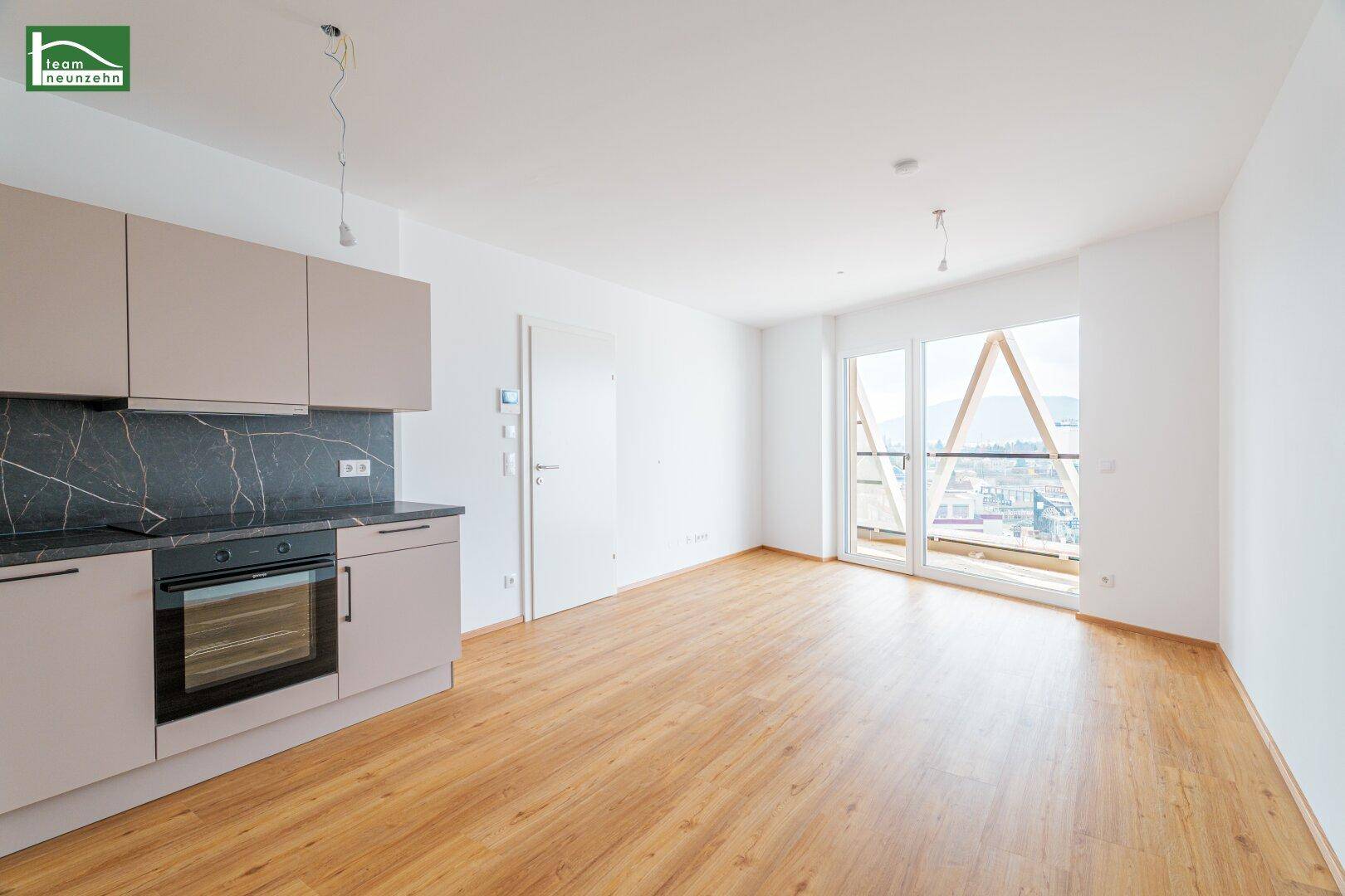 Heller offener Wohnbereich mit moderner Küchenzeile, Holzboden und Zugang zum Balkon.
