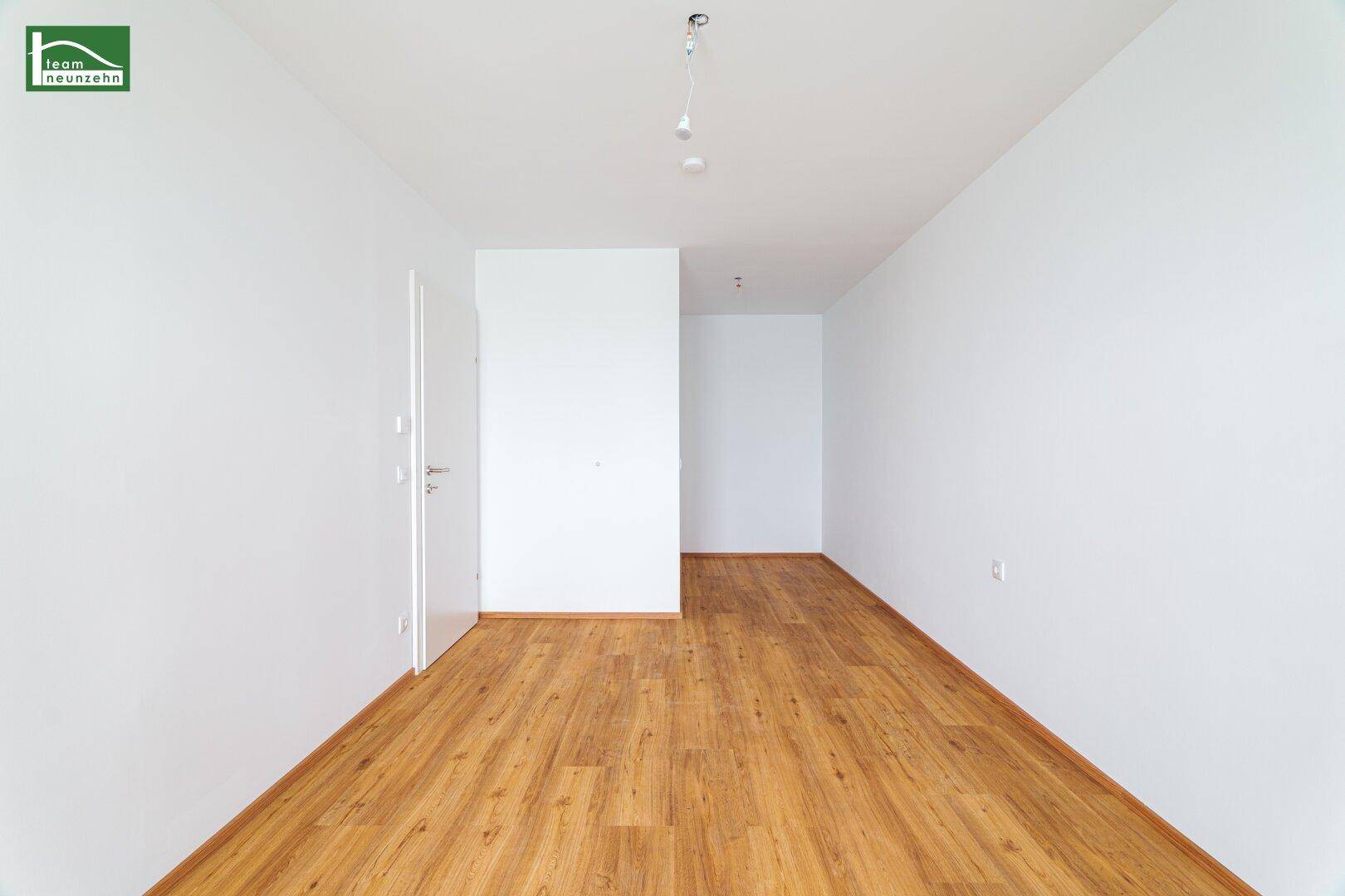 Langer, heller Raum mit Holzboden und weiß gestrichenen Wänden, ideal für einen Flur oder Wohnbereich.
