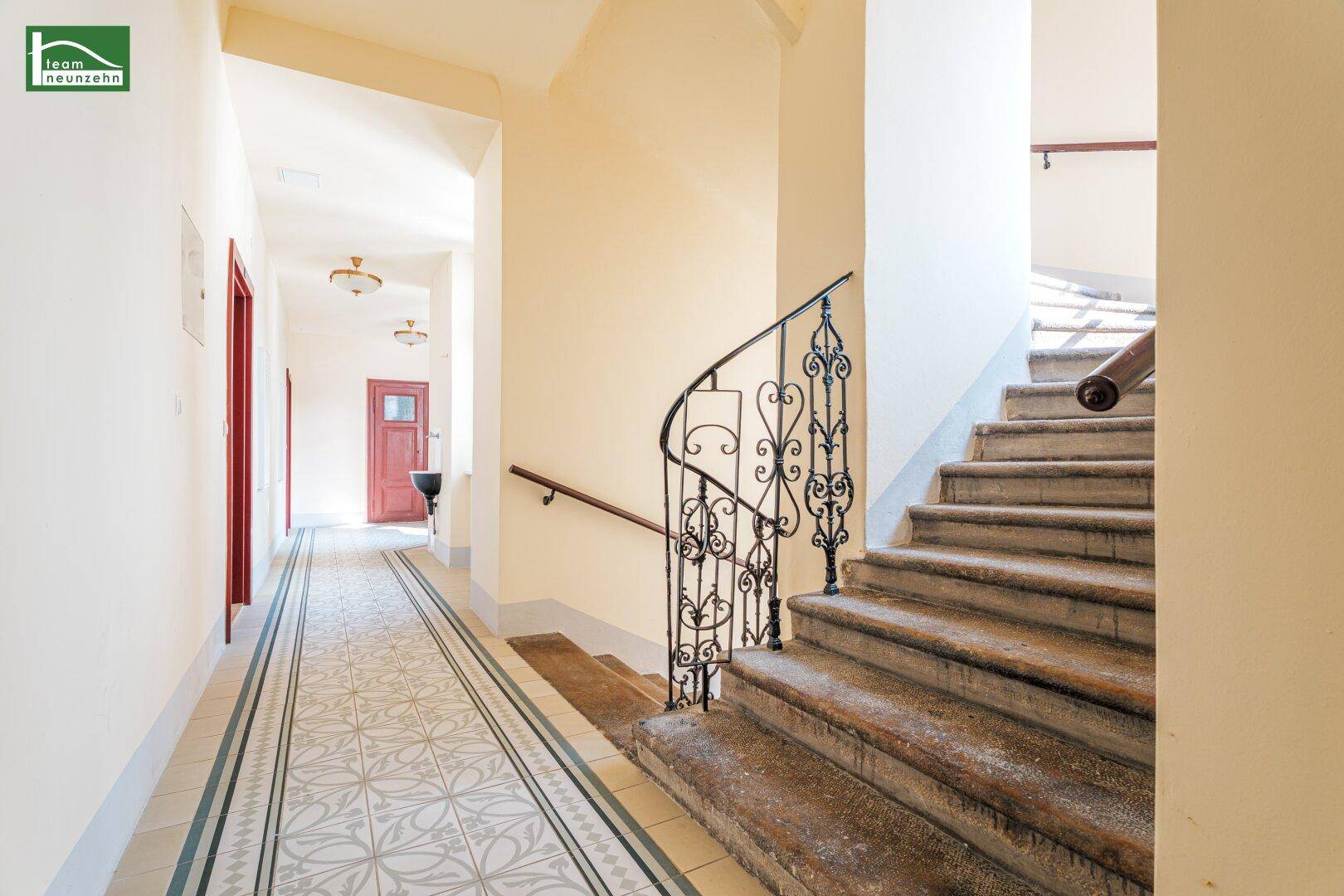 Heller Hausflur mit gemusterten Fliesen, einer geschwungenen Treppe und schmiedeeisernem Geländer.