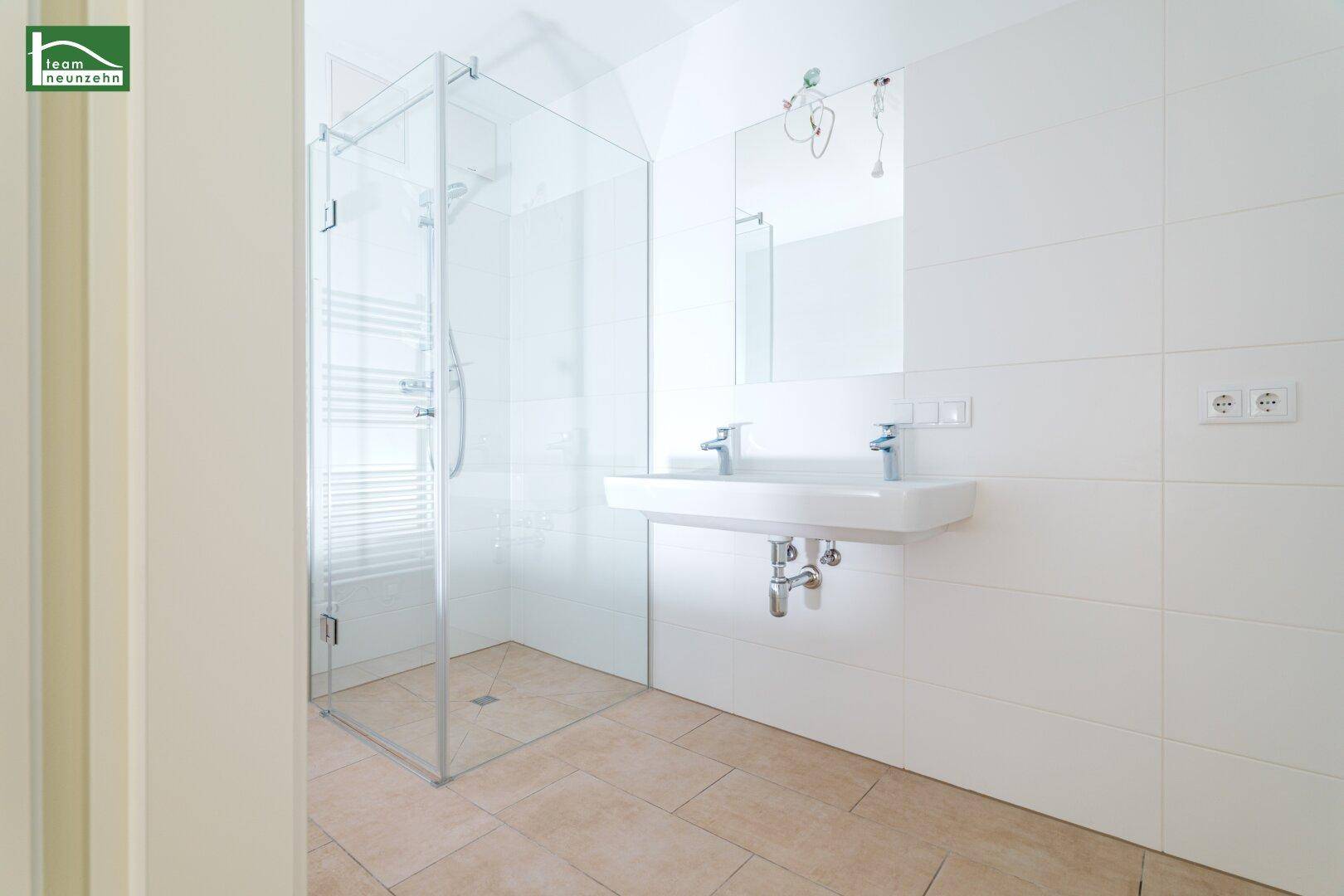 Modernes Badezimmer mit Doppelwaschbecken, großer Dusche und hellen Fliesen in zeitgemäßem Design.