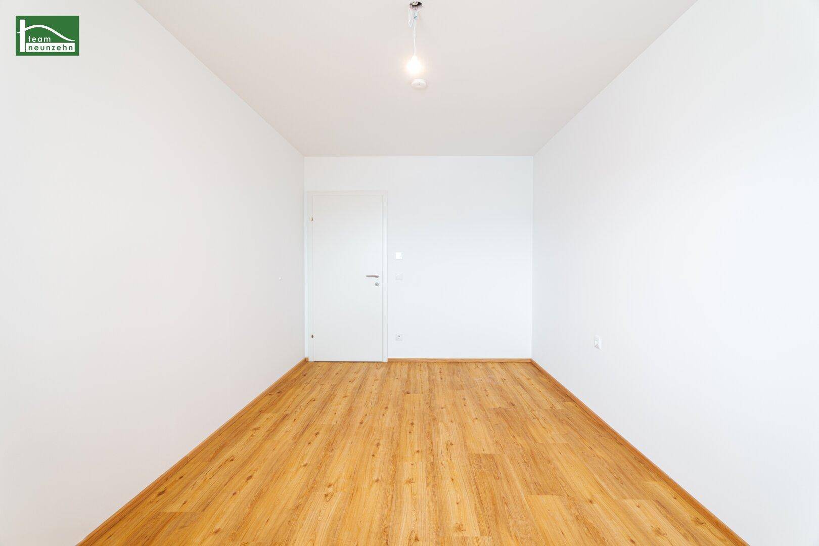 Leeres, helles Zimmer mit Laminatboden und weißer Tür, ideal für Schlaf- oder Arbeitszimmer.