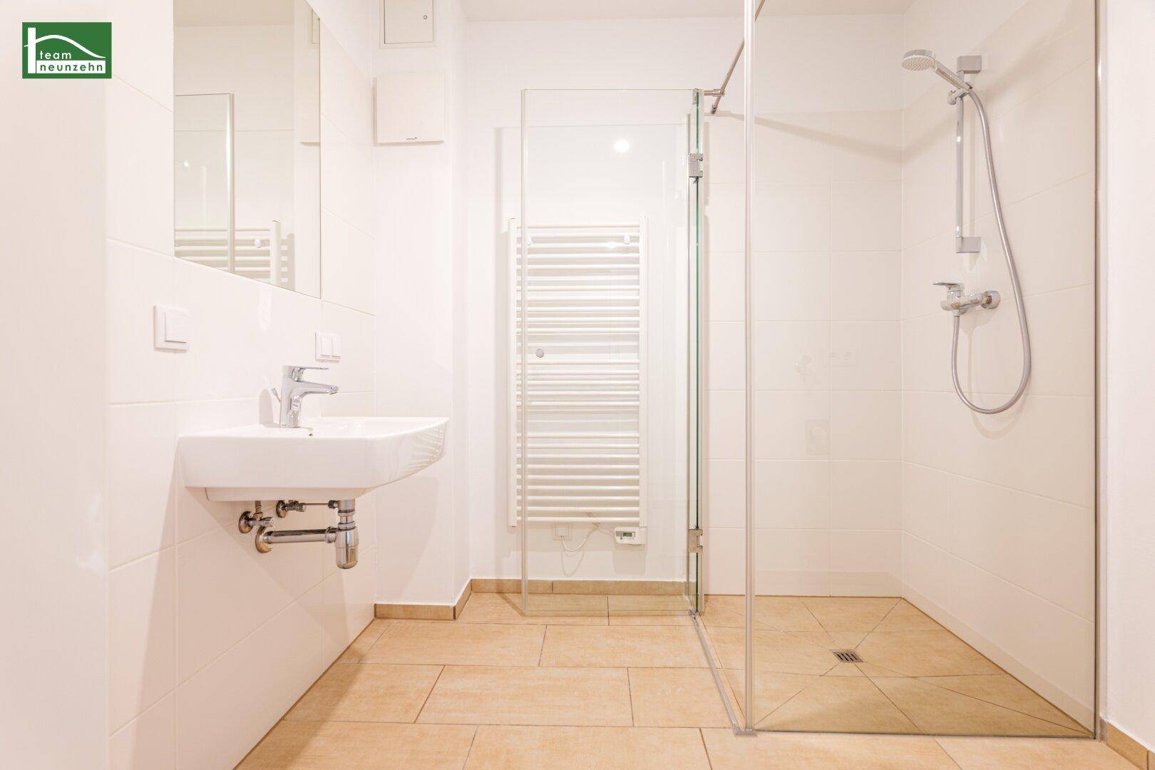 Modernes Badezimmer mit ebenerdiger Dusche, Wandwaschbecken und beheiztem Handtuchhalter.