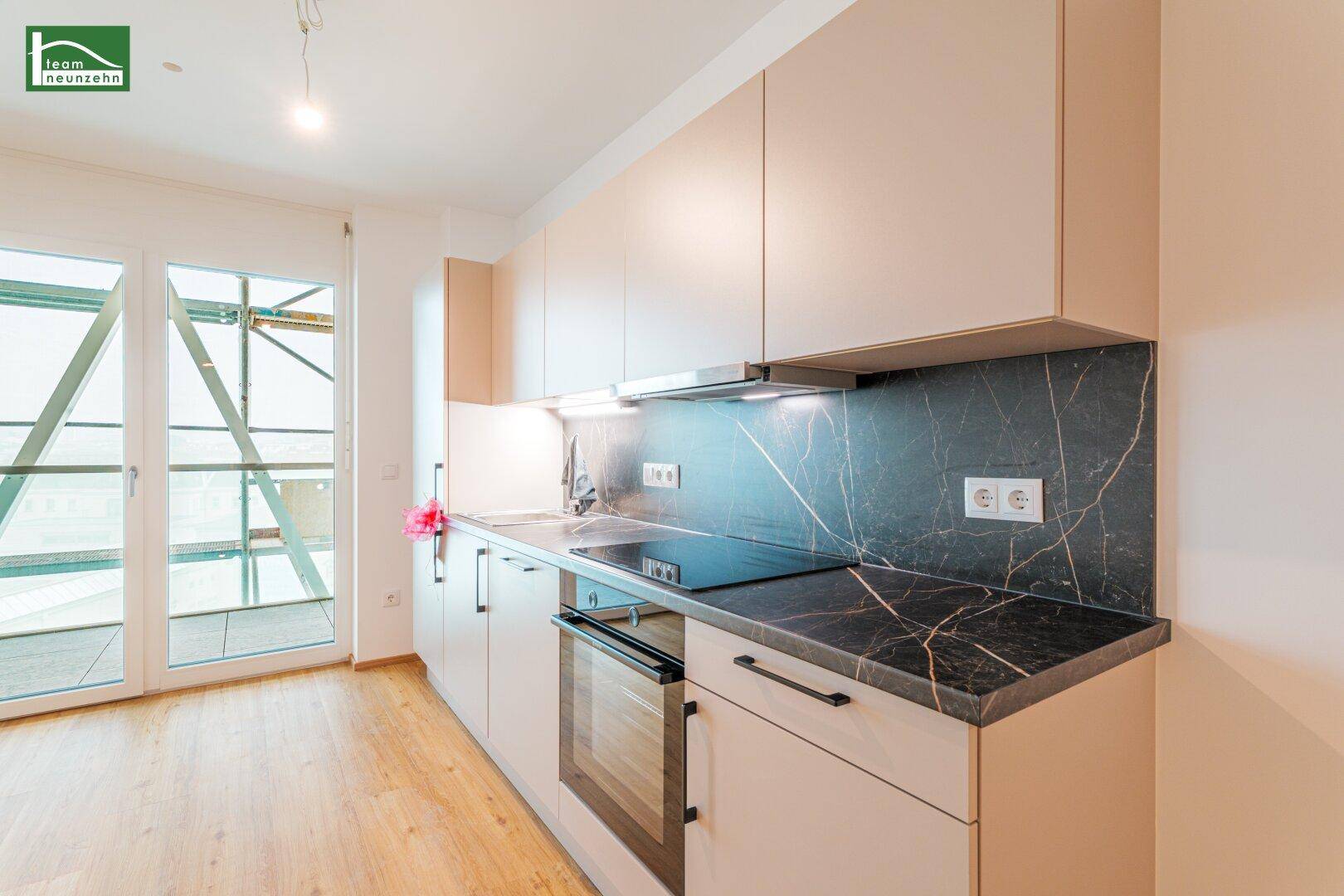 Moderne Küche mit beigefarbenen Schränken, dunkler Arbeitsplatte und Zugang zu einem Balkon.