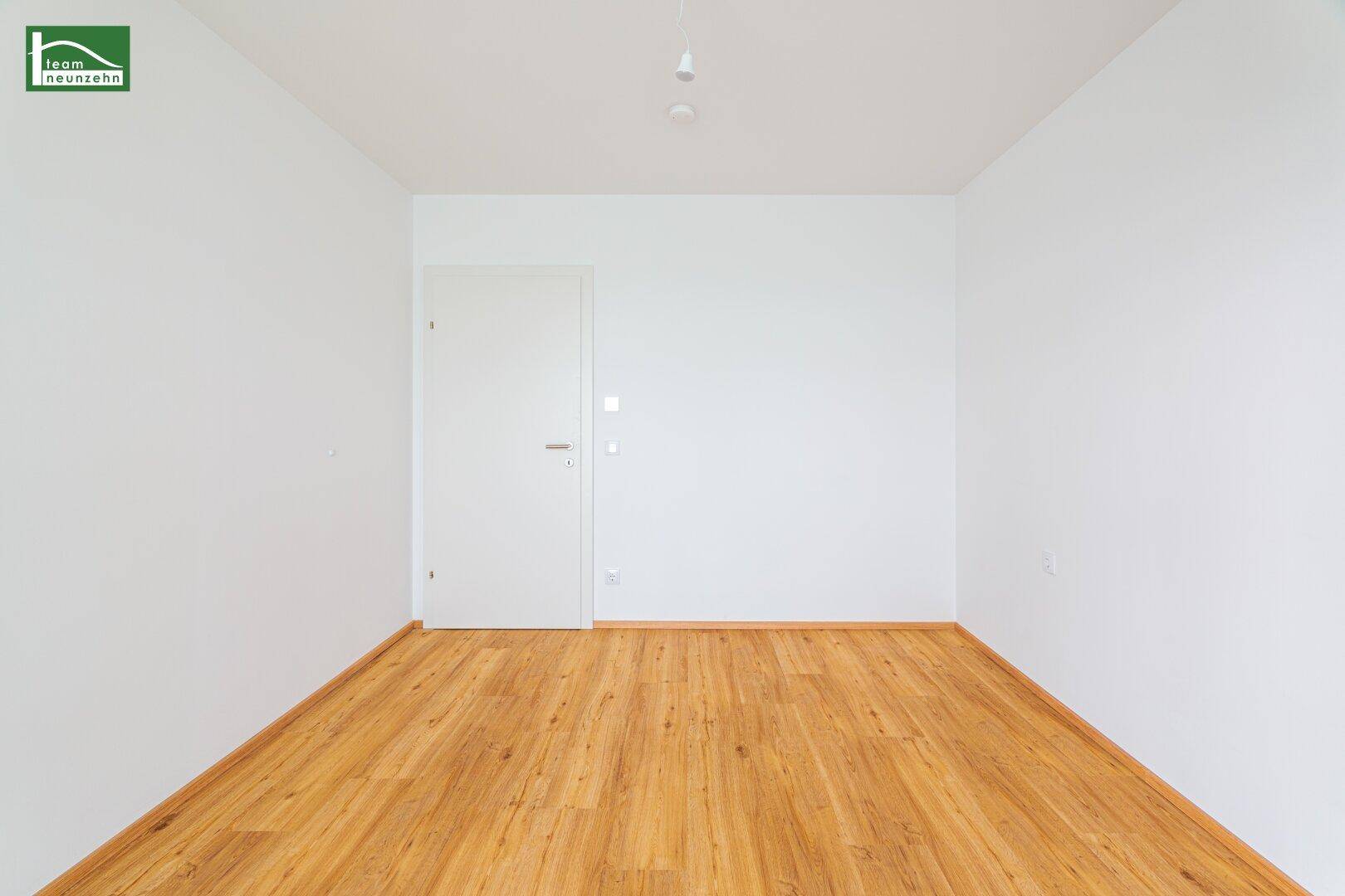 Leerer, heller Raum mit Holzboden und weißer Tür, bereit für neue Bewohner.