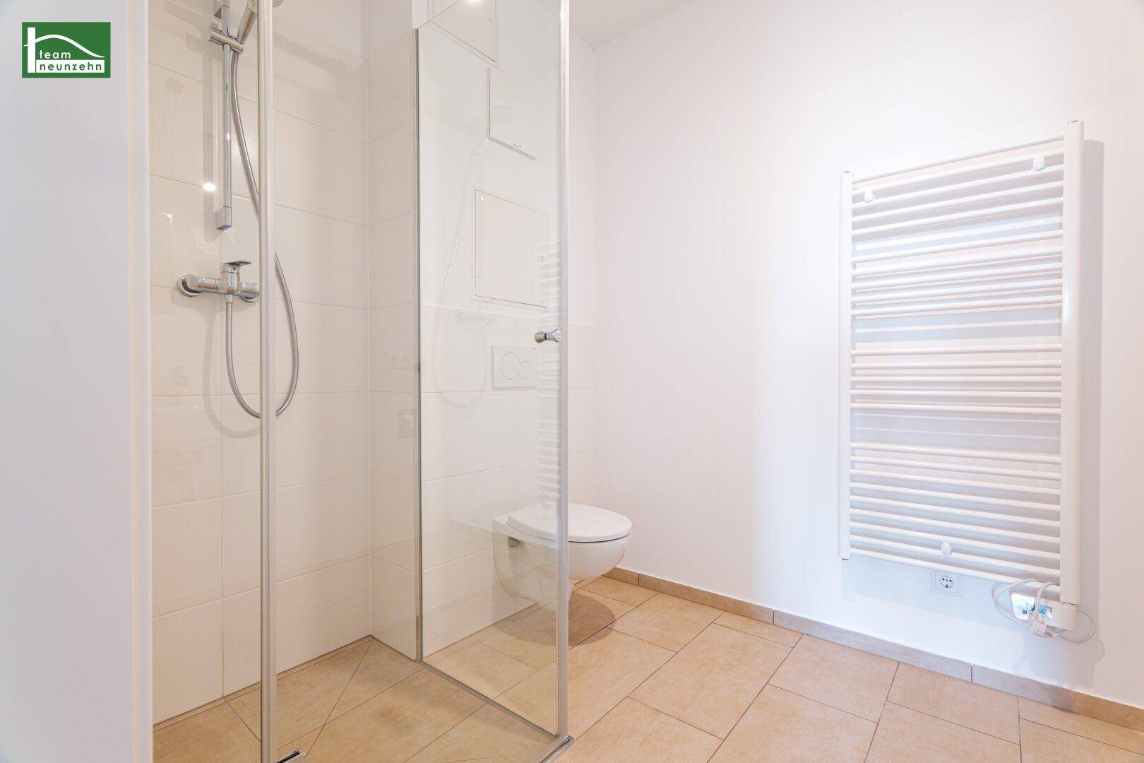 Helles Badezimmer mit ebenerdiger Dusche, wandhängendem WC und beheiztem Handtuchhalter.