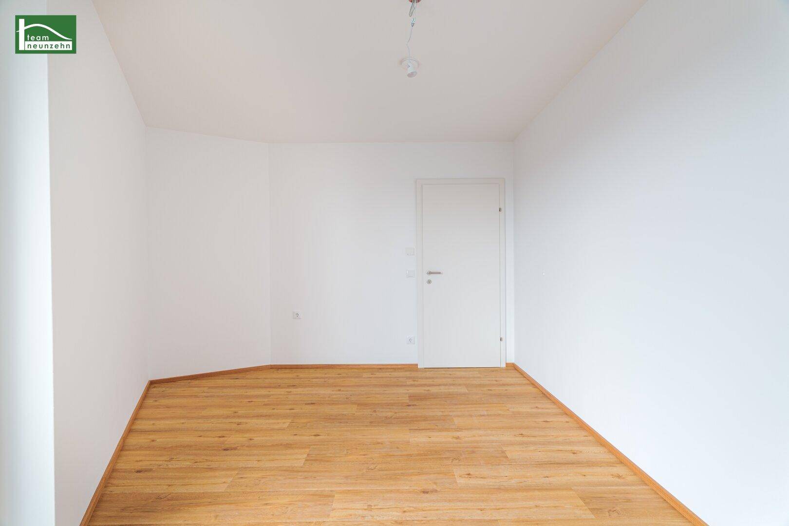 Leeres Zimmer mit hellem Laminatboden und weiß gestrichenen Wänden.
