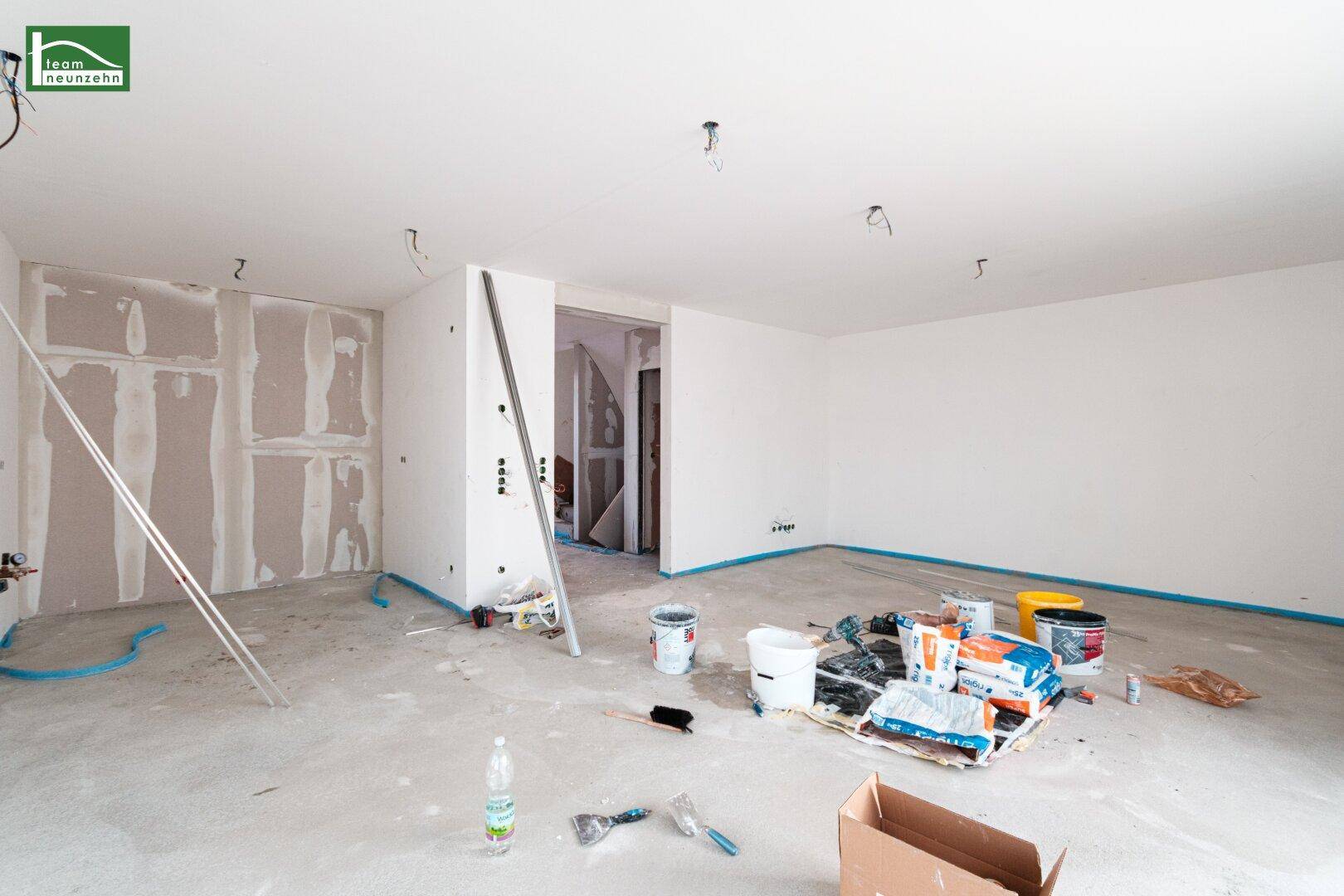Offener Wohnbereich im Rohbau mit Trockenbauwänden und Betonboden, bereit für den Ausbau.