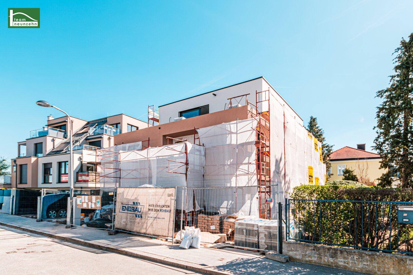 Moderner Neubau im Bauzustand mit Gerüst und angrenzenden Gebäuden an einer Straße.