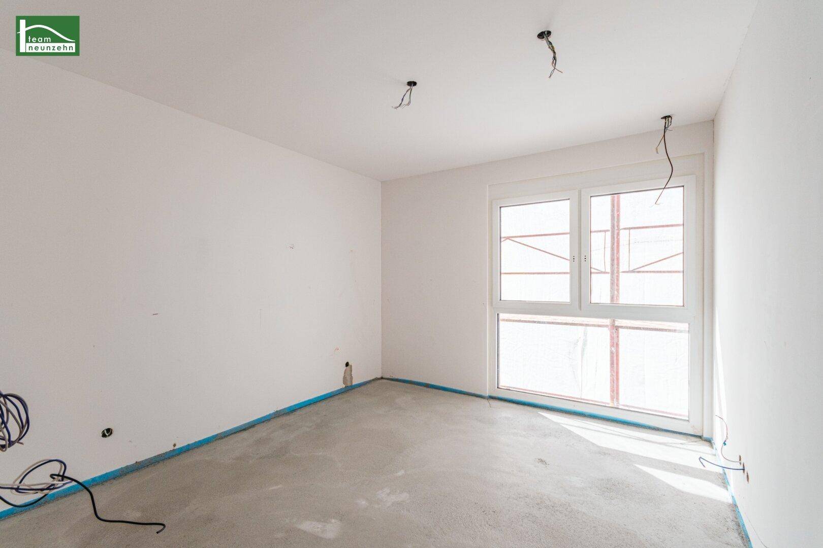 Helles Zimmer mit großem Fenster und Betonboden, bereit für den Innenausbau.