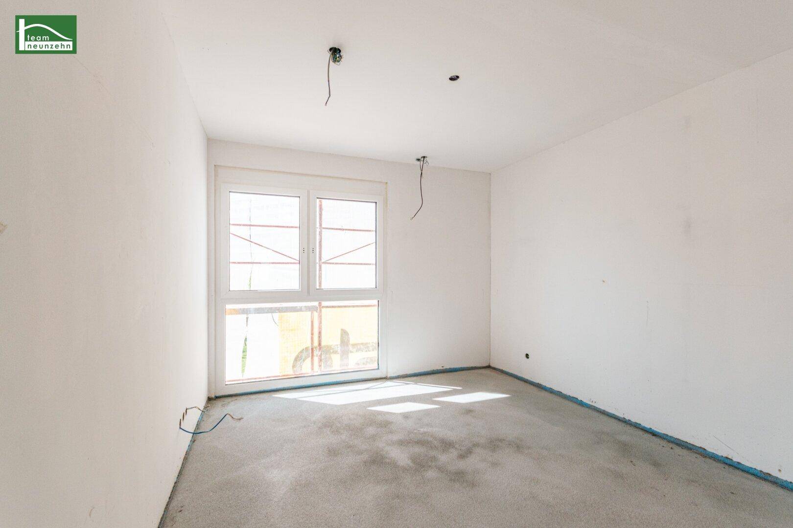 Leeres Zimmer mit großem Fenster und Betonboden, bereit für den Innenausbau.