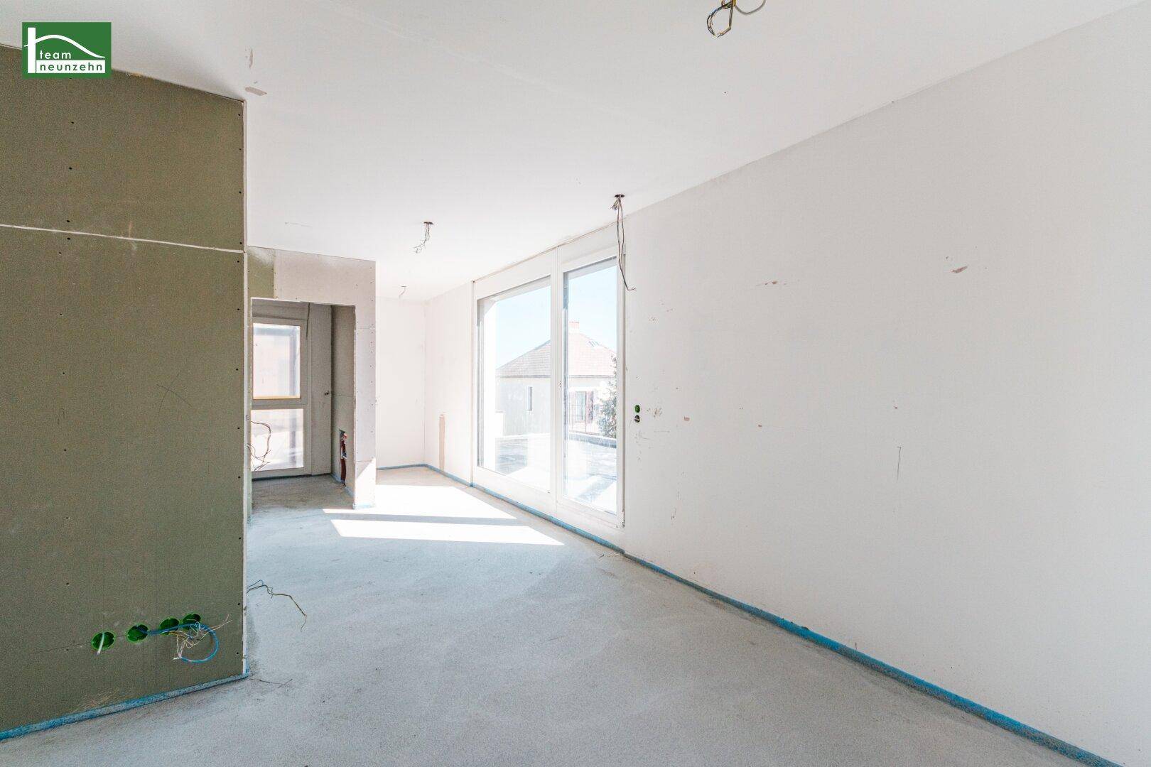 Offener Rohbau mit großen Fenstern und Betonboden, bereit für den Innenausbau.