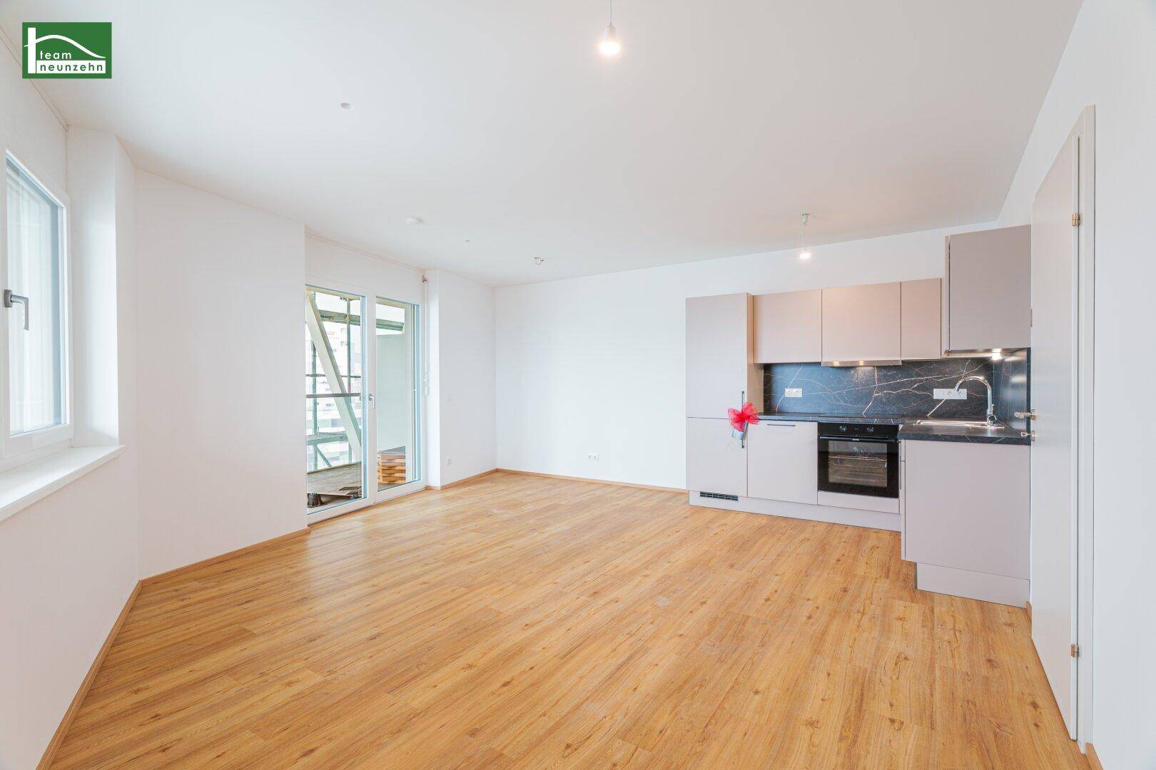 Heller offener Wohnbereich mit integrierter Küche, Parkettboden und Zugang zum Balkon.