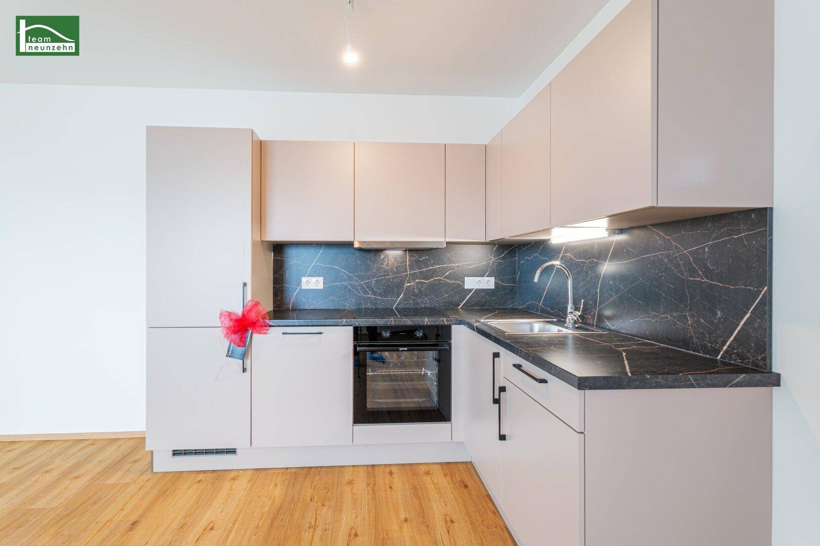 Moderne Einbauküche mit hellgrauen Fronten, dunkler Arbeitsplatte und integriertem Backofen.