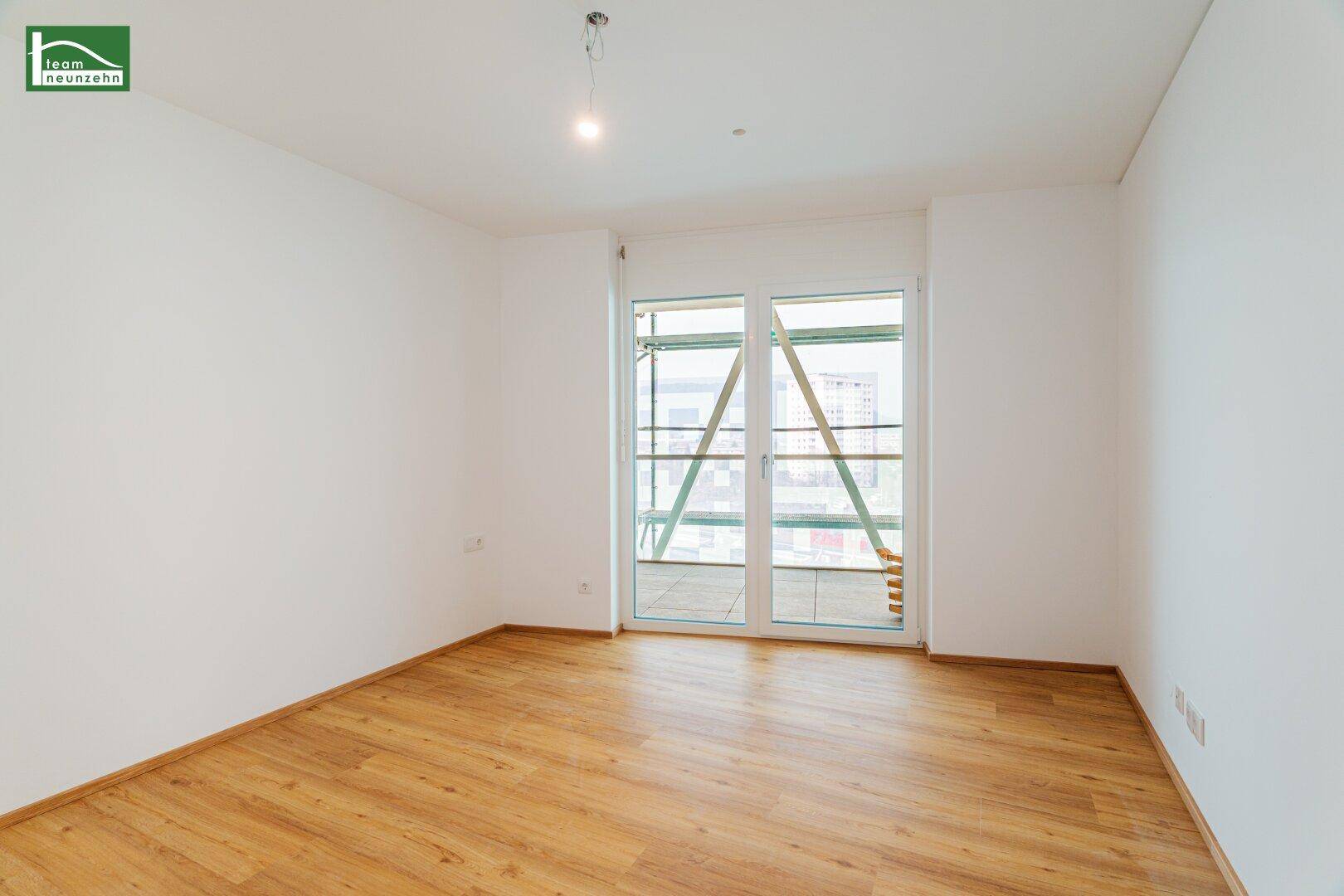Helles, leeres Schlafzimmer mit Holzboden und Zugang zu einem Außenbereich.
