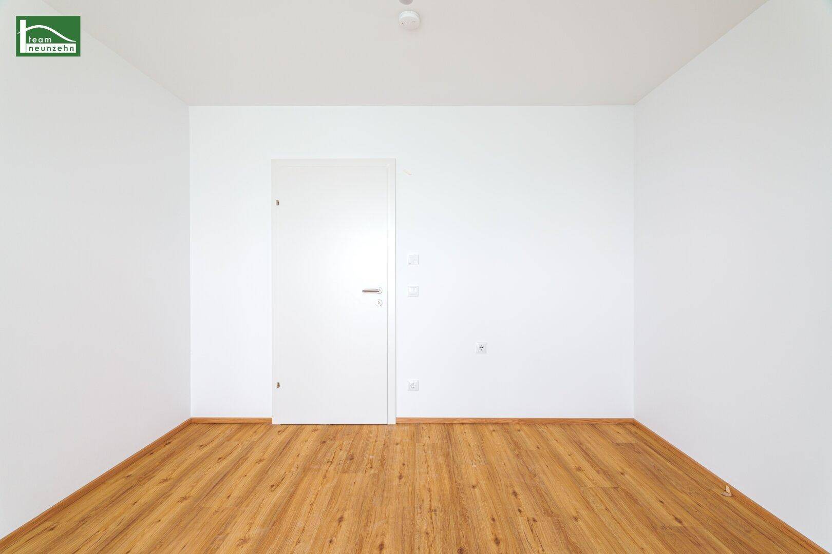 Leeres Zimmer mit Holzboden, weißen Wänden und einer modernen weißen Tür.