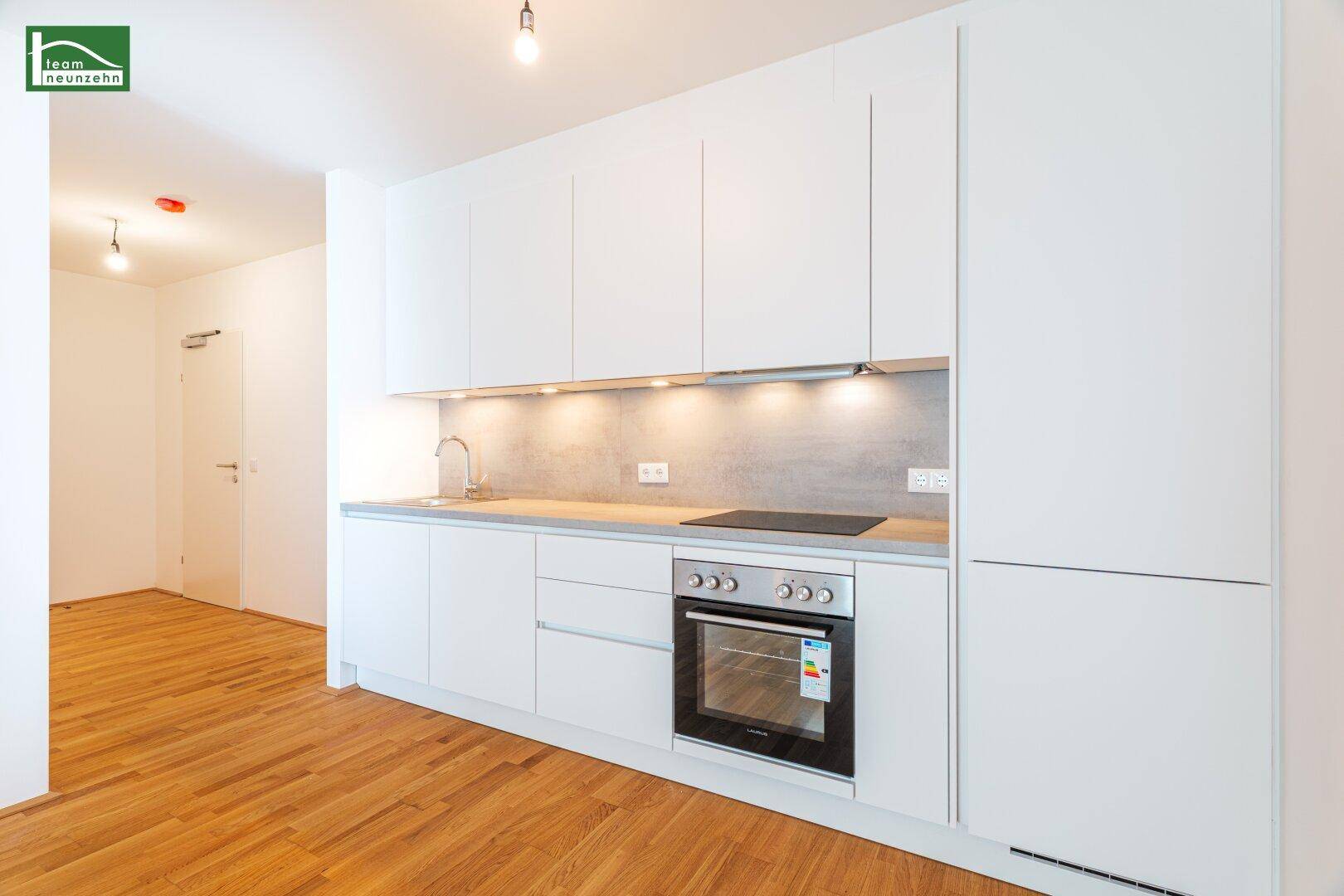 Moderne Küchenzeile mit weißen Schränken, integriertem Backofen und Induktionskochfeld.
