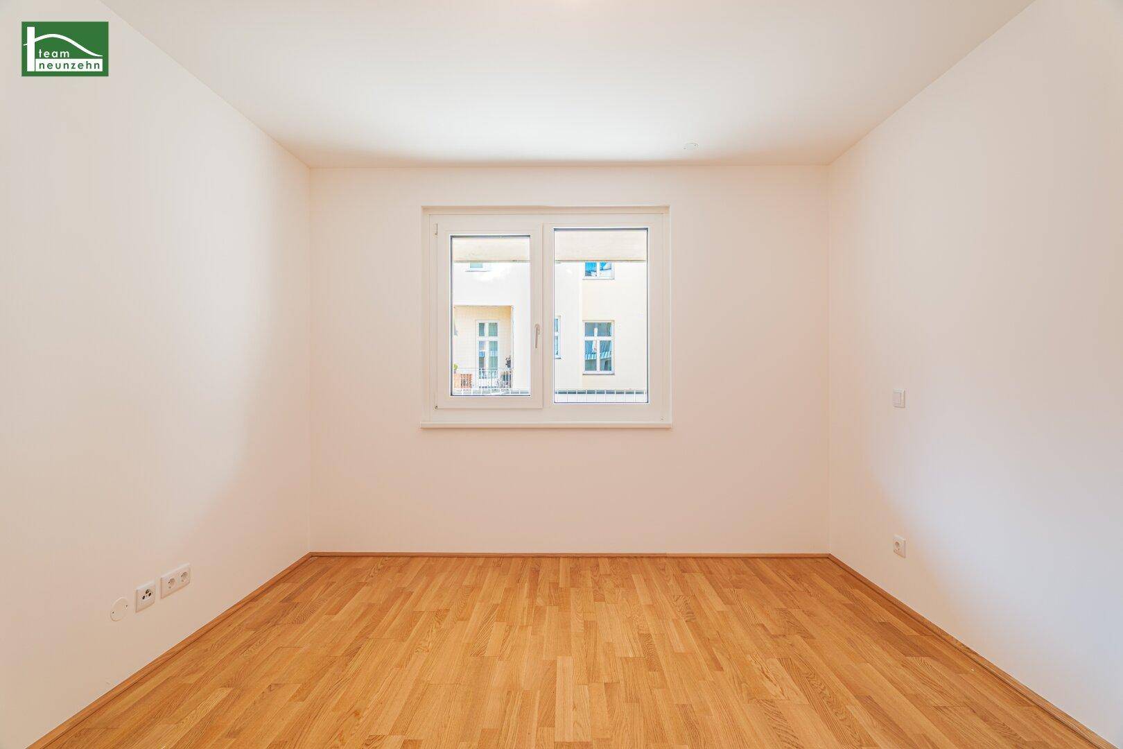 Leeres Zimmer mit hellem Parkettboden und einem Fenster zum Innenhof, ideal für Schlafzimmer oder Büro.