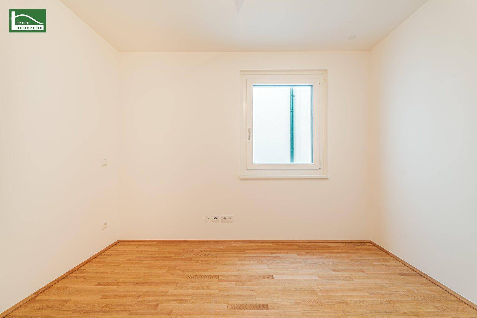 Helles Zimmer mit Parkettboden und einem Fenster, das einen Blick nach draußen ermöglicht.