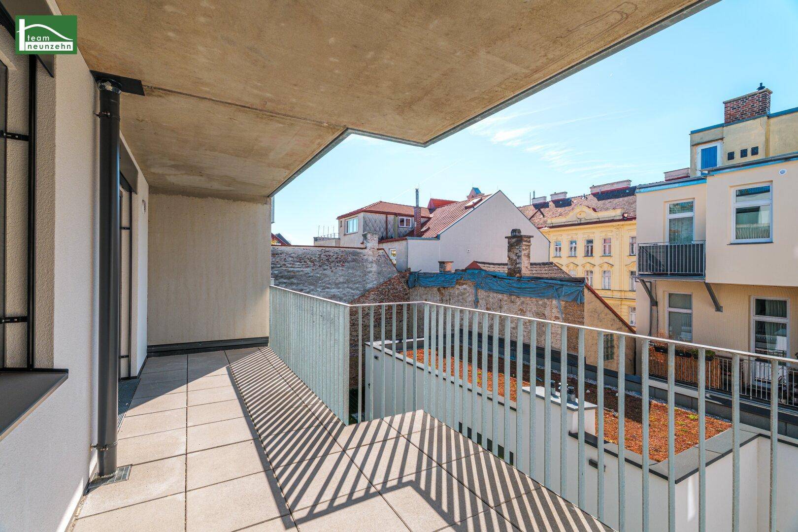 Geräumiger Balkon mit Fliesenboden und Metallgeländer, bietet einen Blick auf die umliegenden Gebäude.