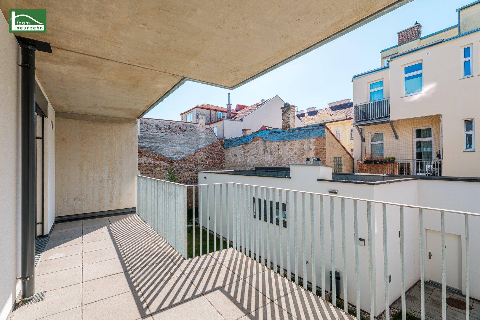 Großer Balkon mit Fliesenboden und weitem Blick über die Dächer der Stadt und angrenzende Gebäude.