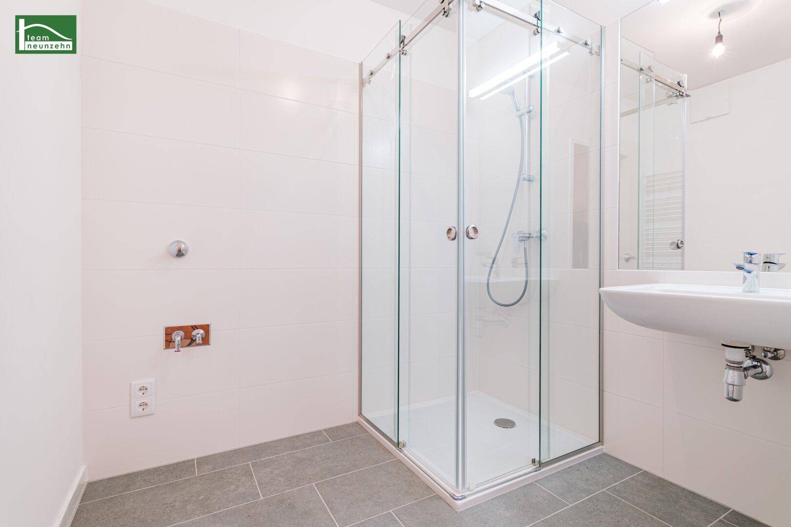 Modernes Badezimmer mit geräumiger Duschkabine, Waschbecken und grauen Fliesen.