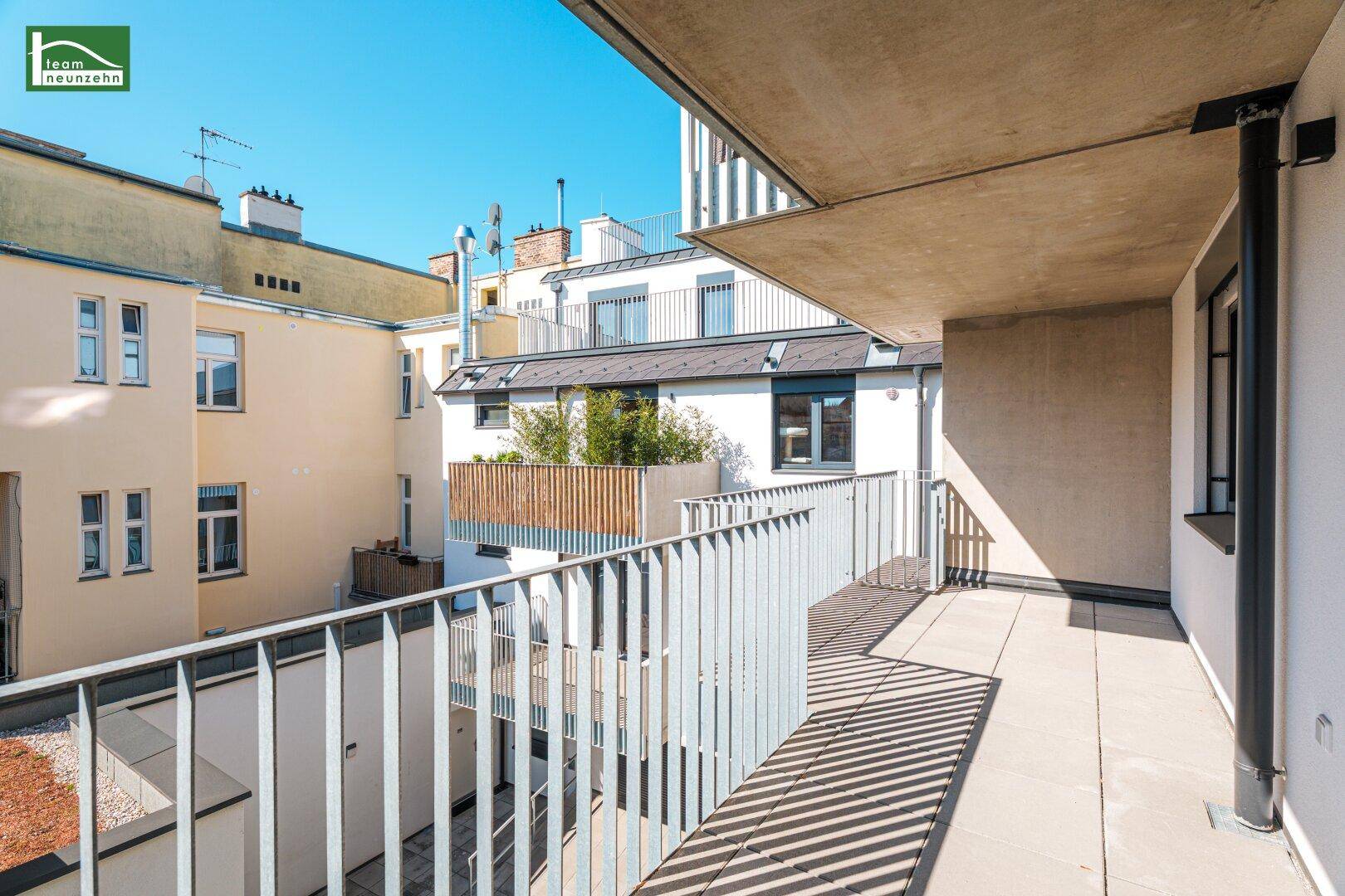 Heller Balkon mit Fliesenboden und Blick auf den ruhigen Innenhof und weitere Gebäude.