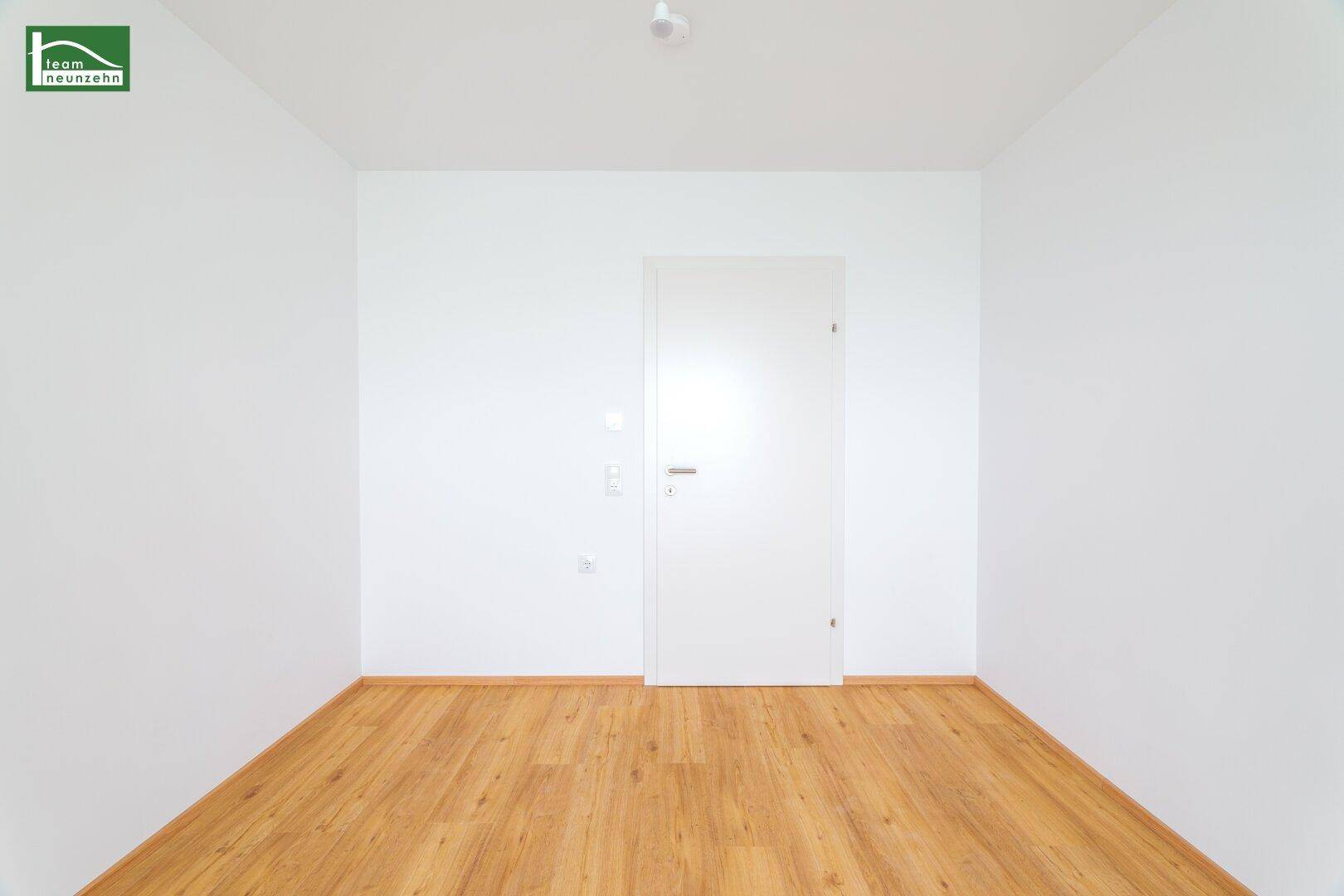 Leeres Zimmer mit Holzboden und weißer Tür, bietet vielseitige Nutzungsmöglichkeiten als Schlafzimmer.