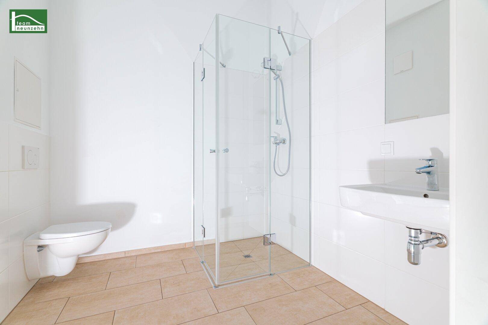 Modernes Badezimmer mit Glasdusche, wandhängendem WC und hellem Fliesenboden.