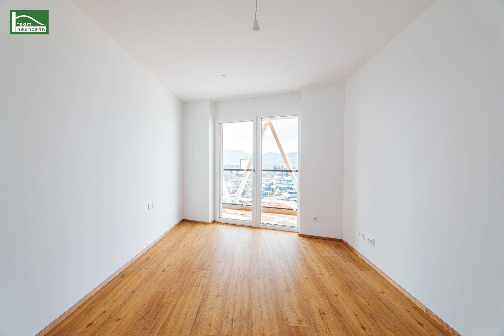 Helles Schlafzimmer mit Holzboden und großen Fenstern, die viel Tageslicht hereinlassen.