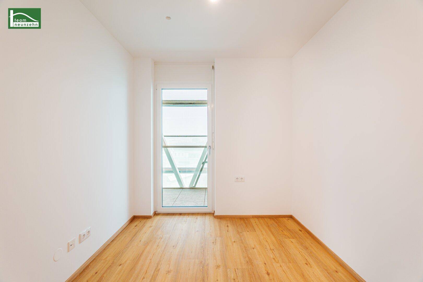 Heller, unmöblierter Raum mit Zugang zu einem Balkon und Parkettboden.