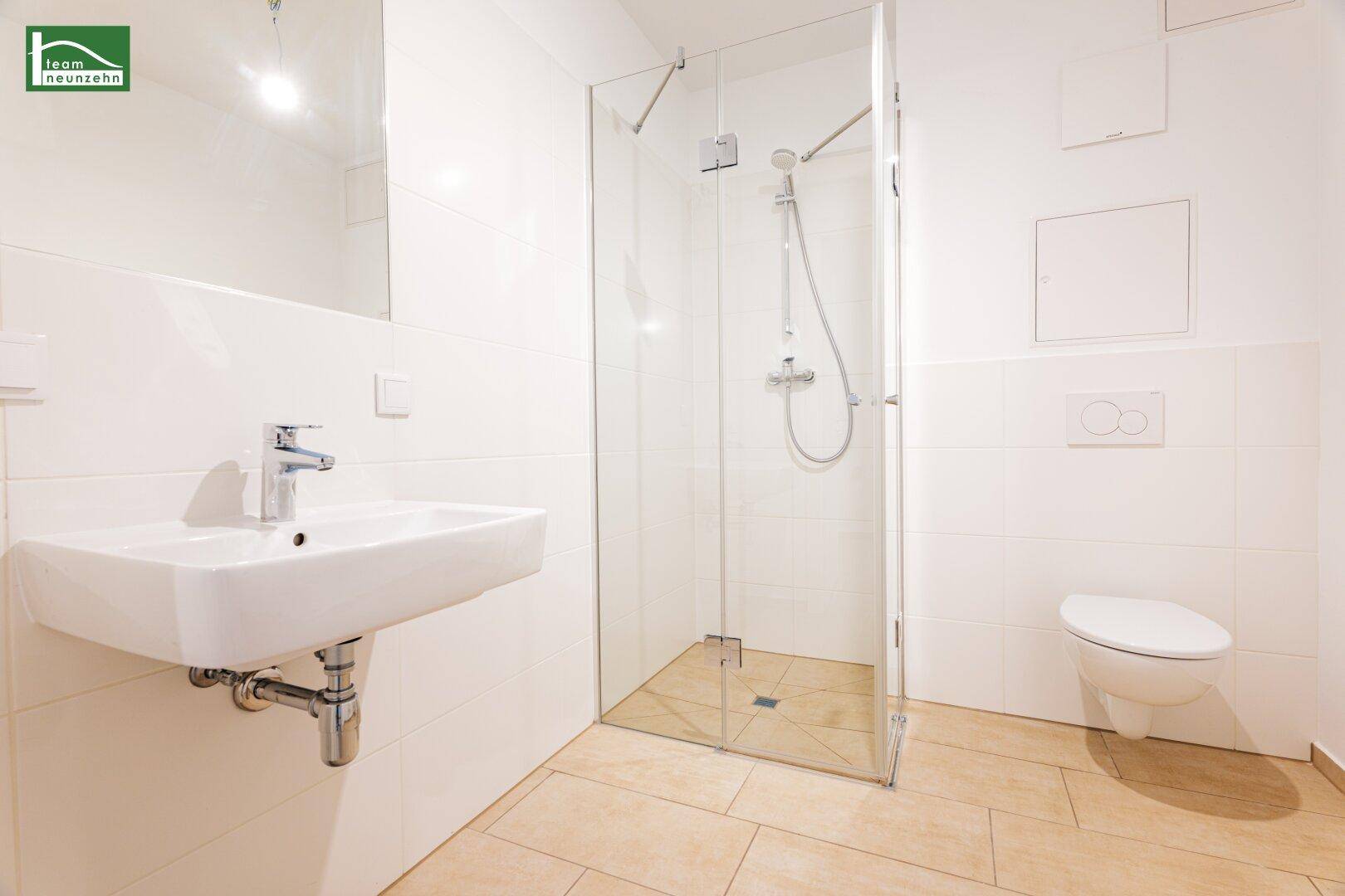 Modernes Badezimmer mit ebenerdiger Dusche, wandhängendem WC und hellem Fliesenboden.